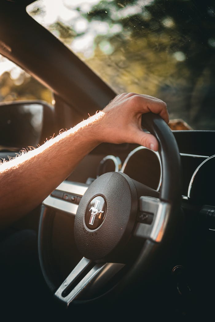 Close-up of a man's hand on a car steering wheel, bathed in warm sunlight.